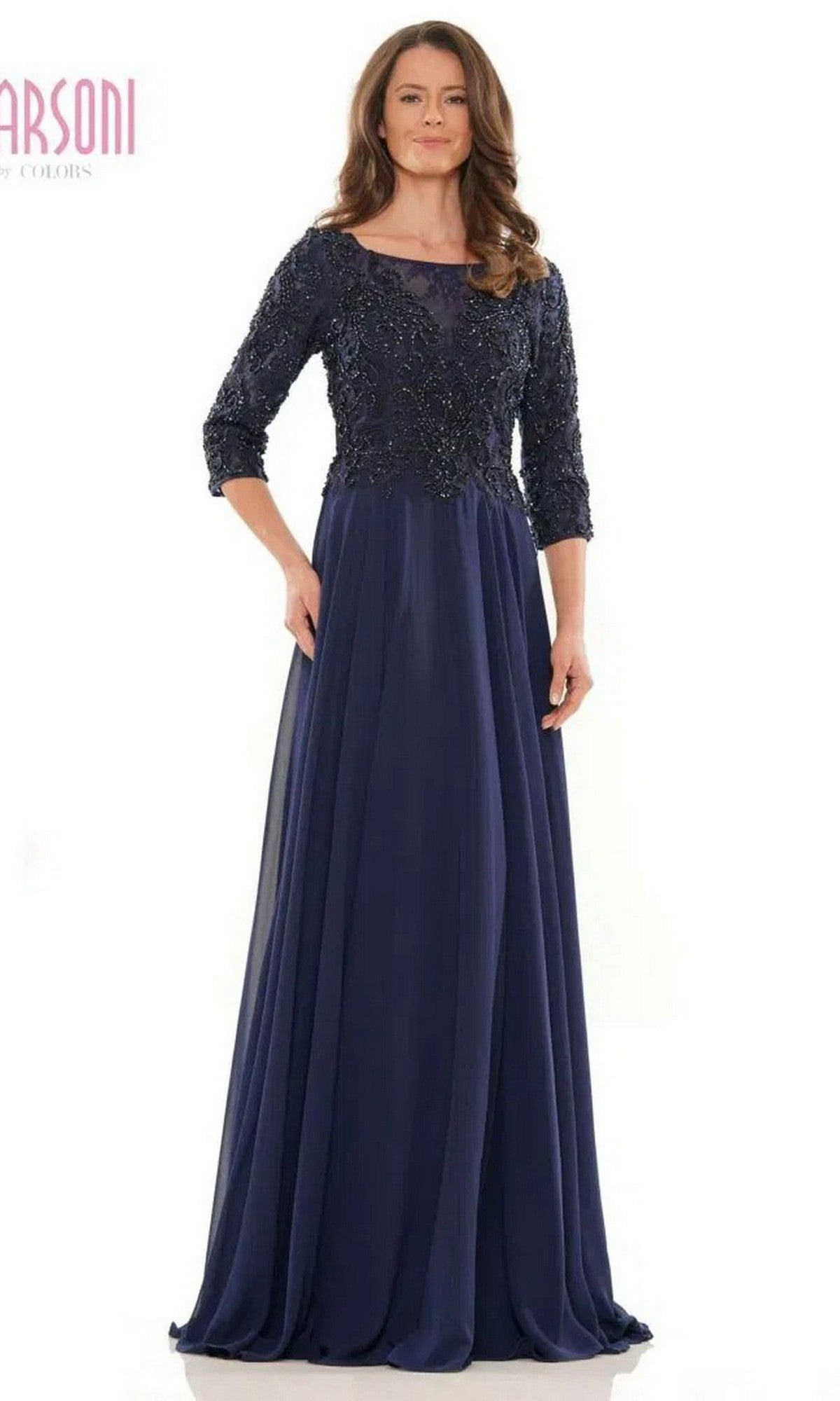 A woman models the Marsoni MV1052 long formal dress in navy, featuring a beaded bodice, three-quarter sleeves, and a floor-length chiffon A-line skirt, standing against a plain white background.